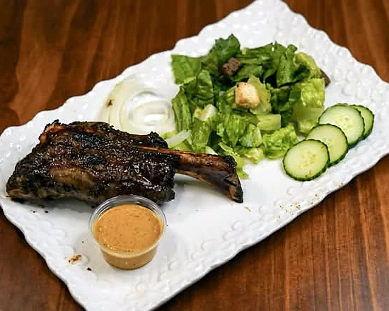 Smoked lamb shank with salad, cucumber slices and dipping sauce on a white platter